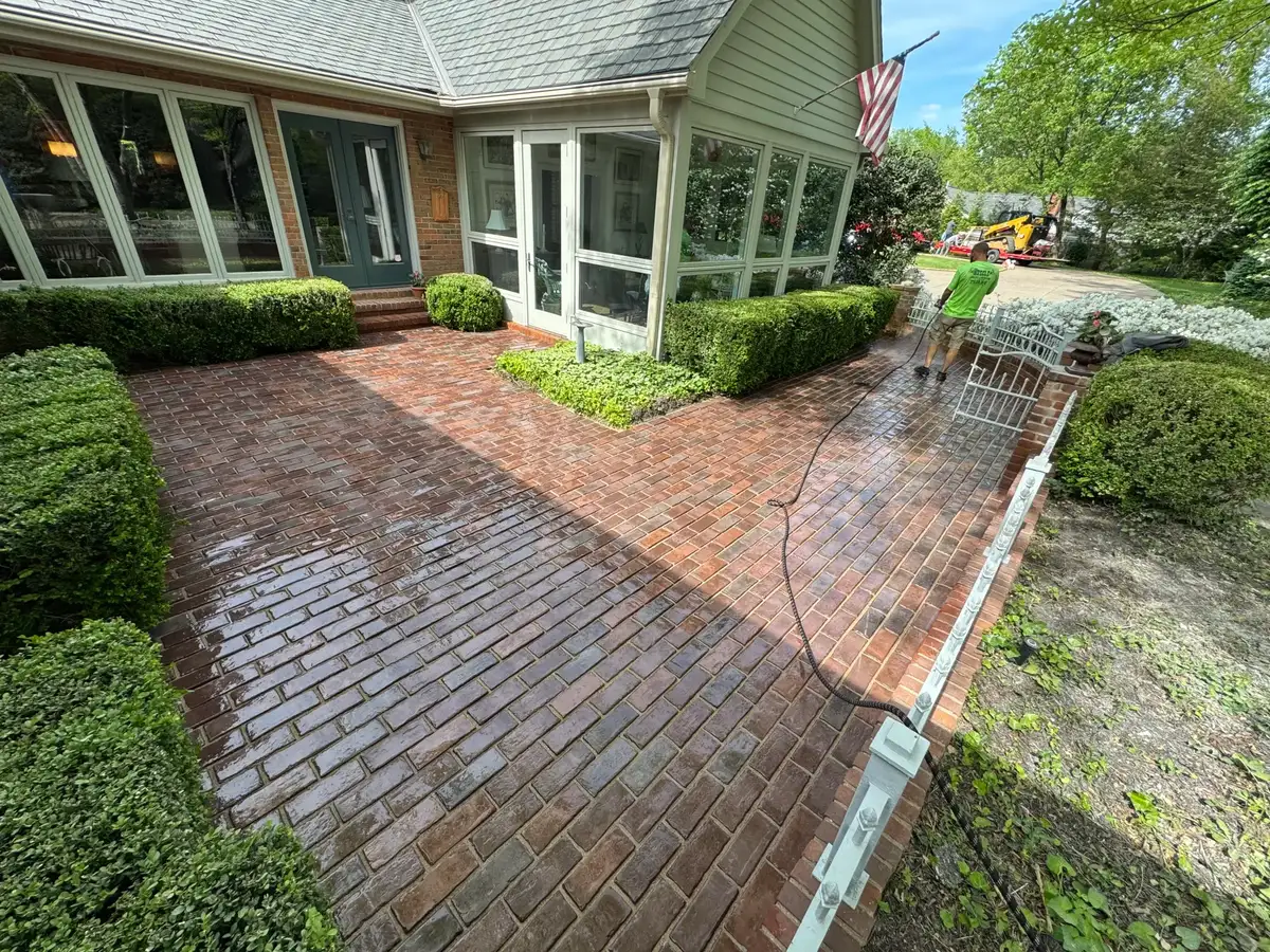 The Muscle team member pressure washing a brick patio with a skid steer staged nearby