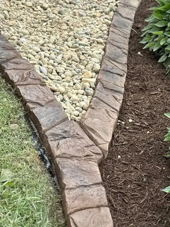 Natural-stone-look stamped curbing beside a gravel bed.