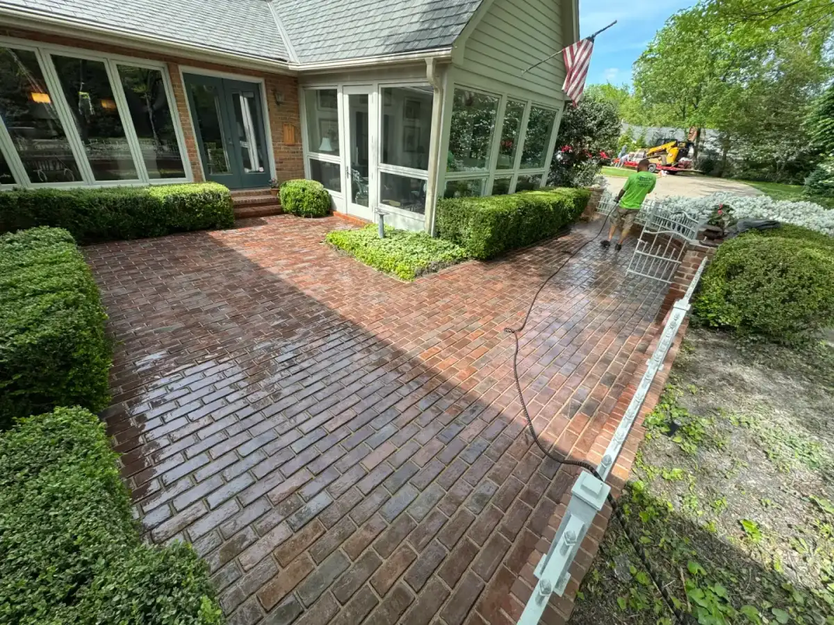 A Muscle team member pressure-washing a brick patio with a skid steer staged nearby.